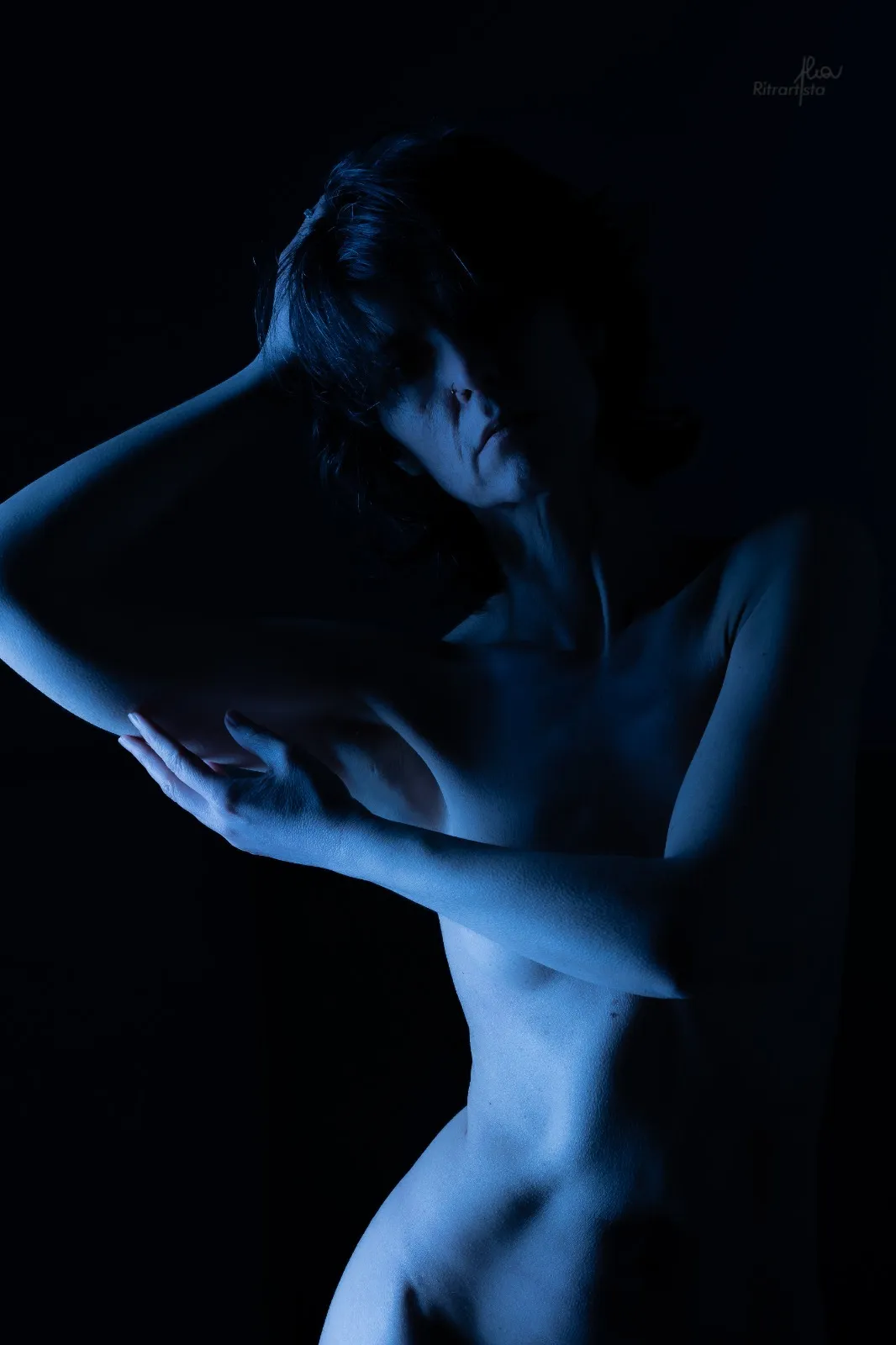 Nudo in luce blu su fondo nero, braccia incrociate