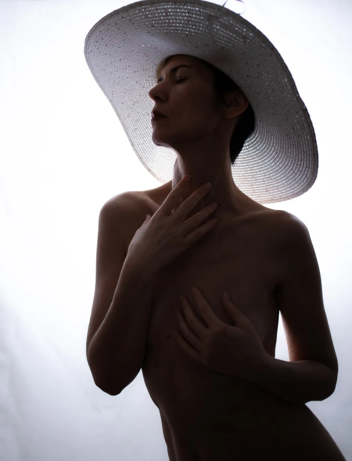 Figura in controluce con grande cappello bianco, occhi chiusi