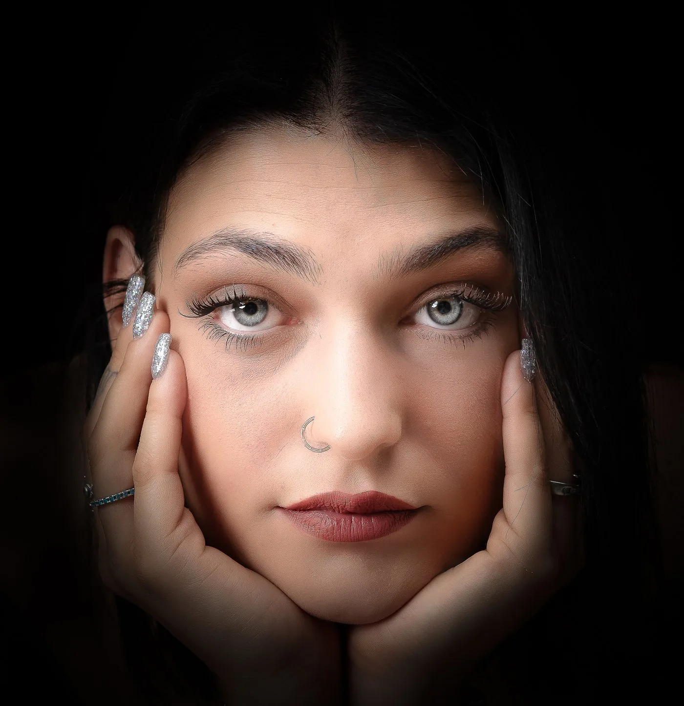 Ritratto d'autore di giovane donna con le mani sul viso, in luce calda su fondo nero